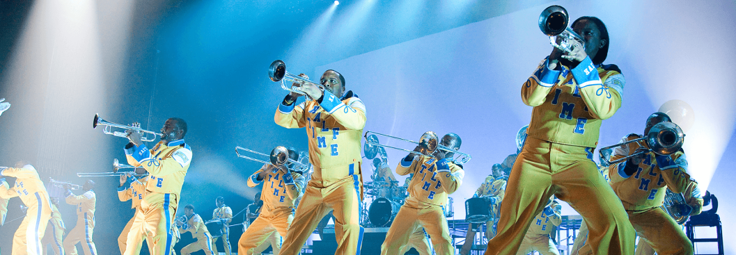 Marching band in yellow costumes. Playing brass instruments.