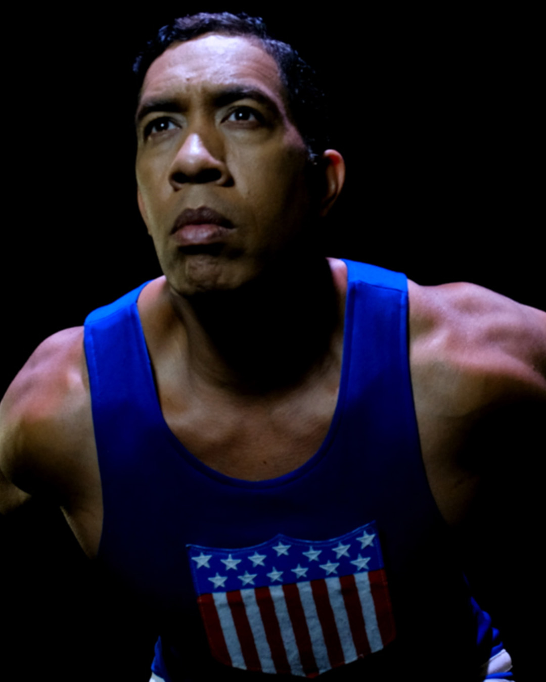An actor wearing a blue tank top with a stars and stripes logo on front