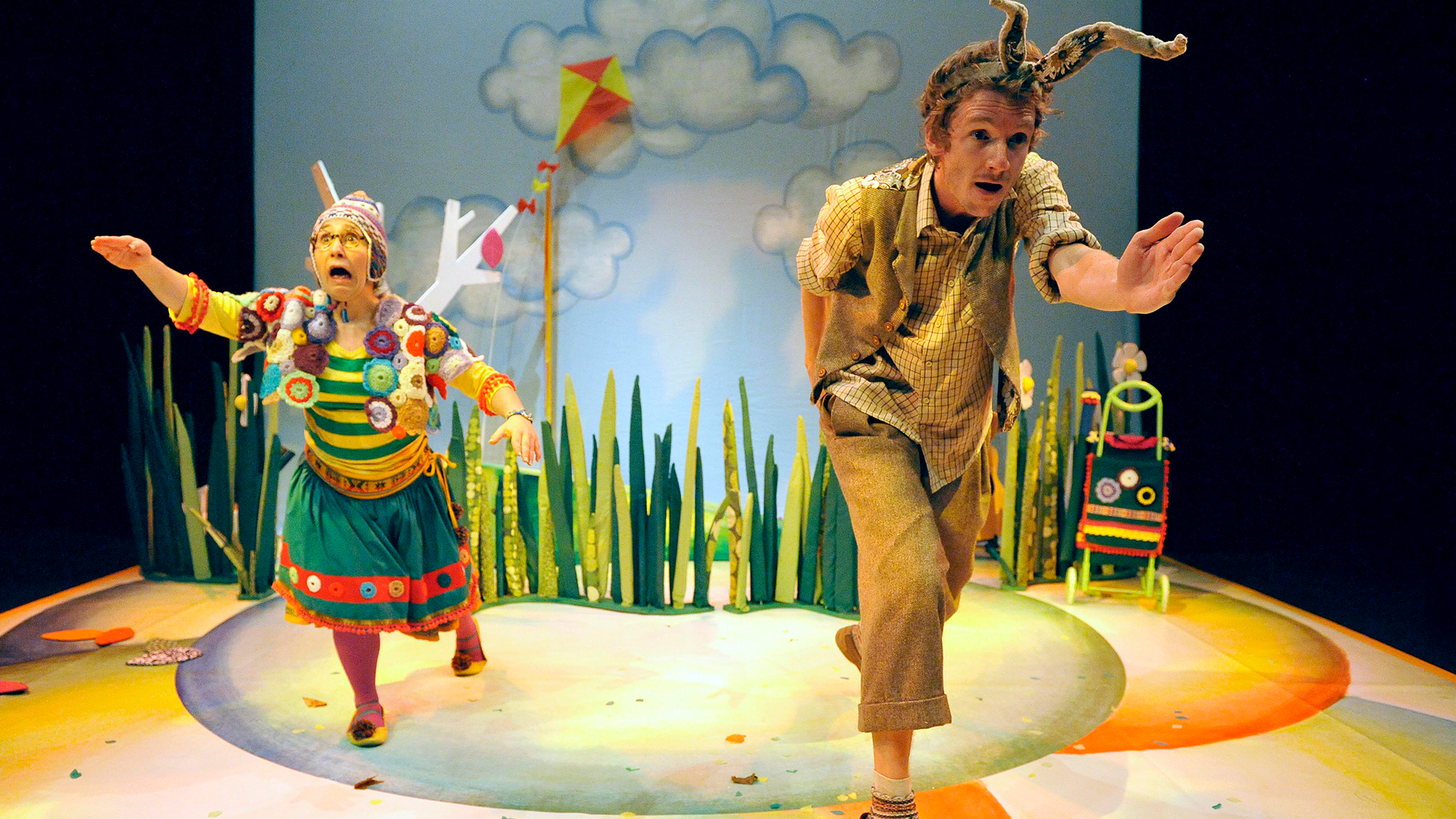 Two people dressed in colorful costumes running with a background of clouds and grass