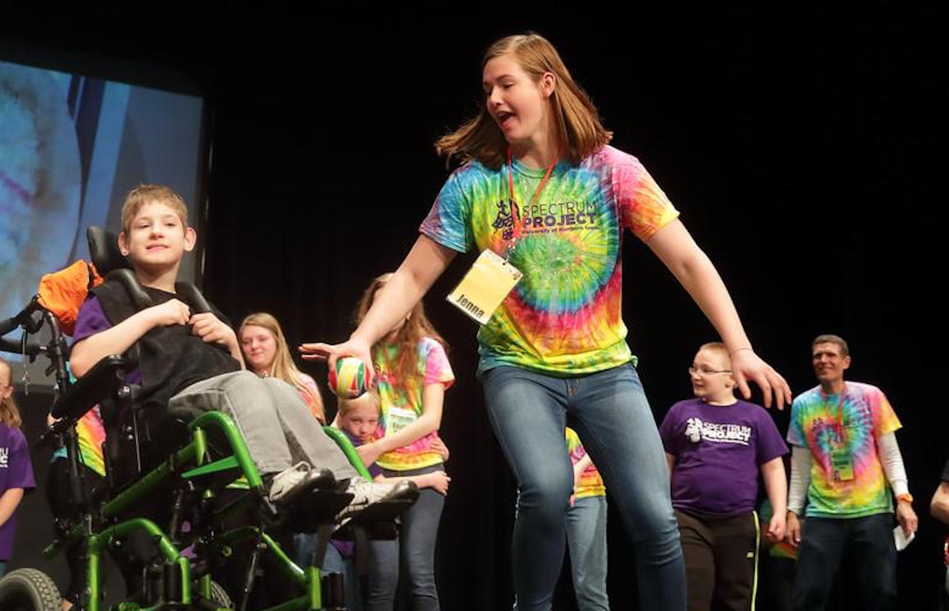 Girl with ball in her hand running around a boy in a wheel chair