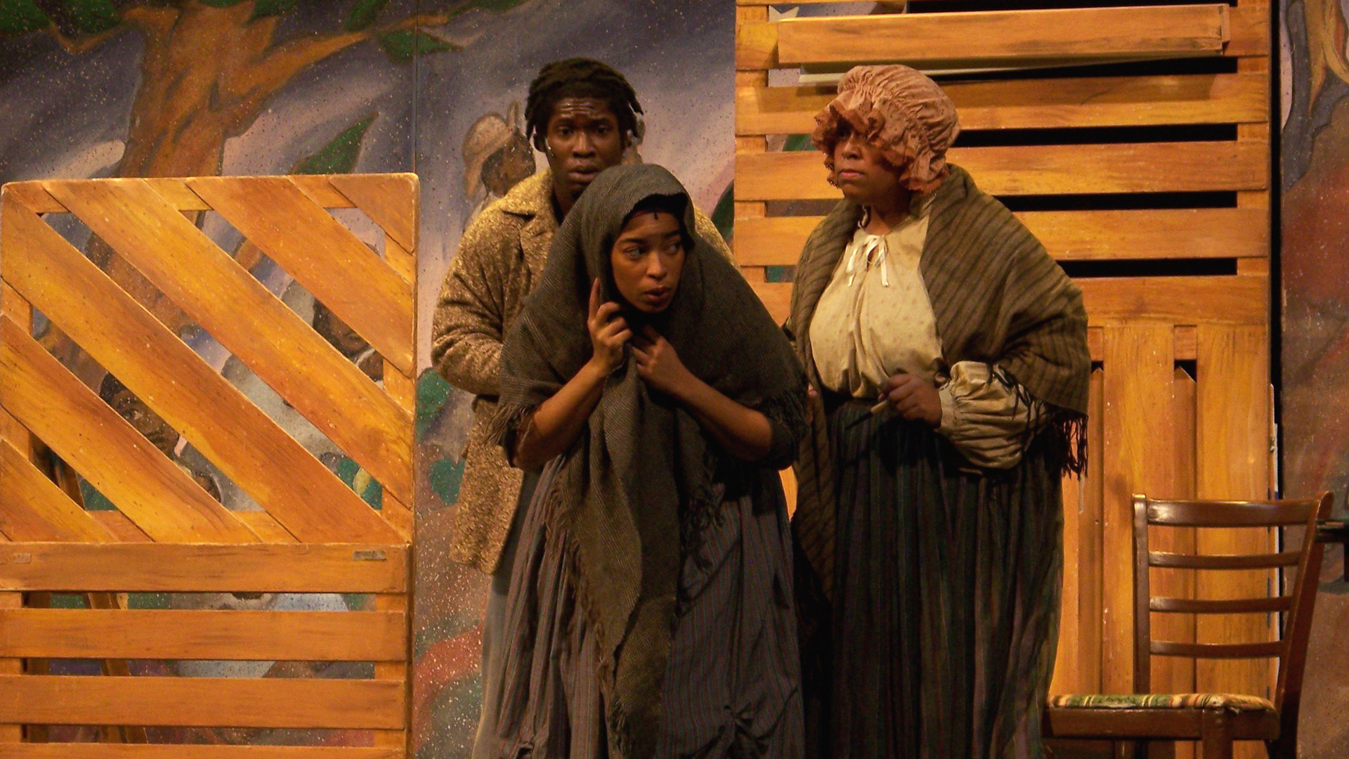 A woman hides with blanket over her head with two people guiding her in the background 