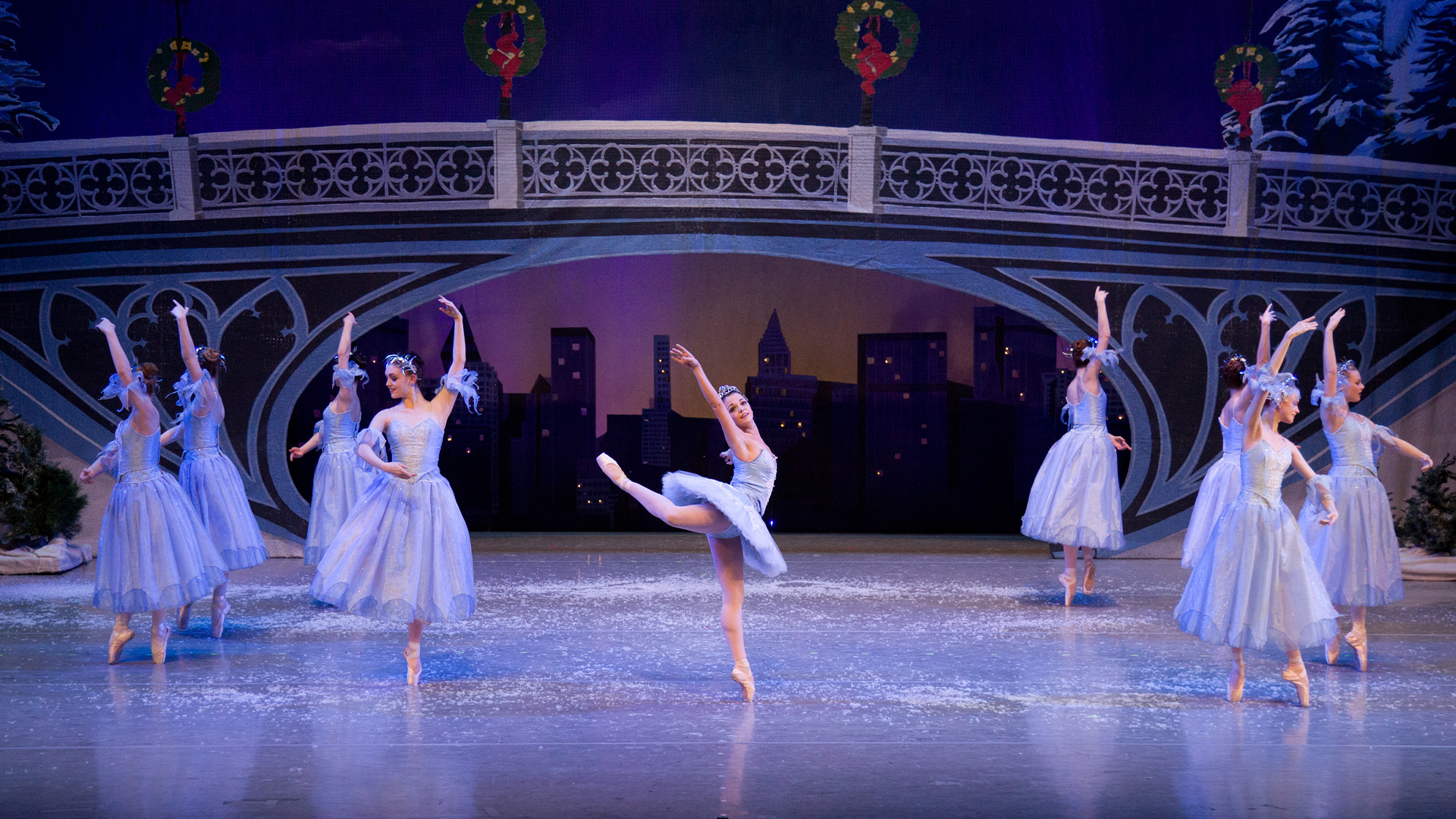 A group of ballet dancers in blue dresses dancing below a bridge