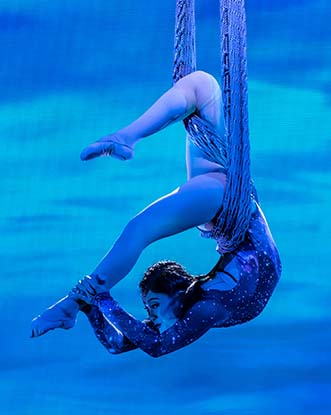A person suspended holding their legs doing gymnastics with a blue background