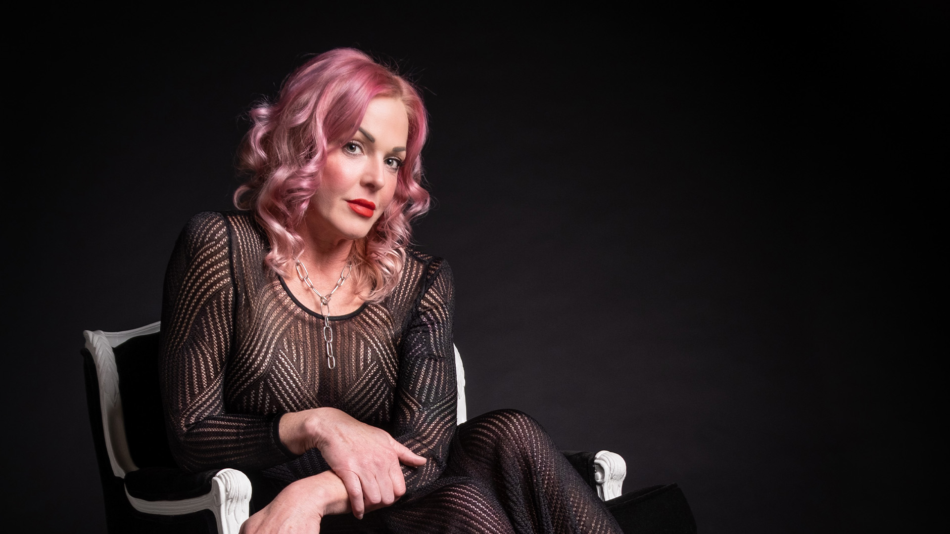 Storm Large sitting a chair with arms overlapping