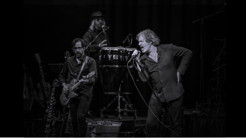 A man singing with a band in the background in black and white