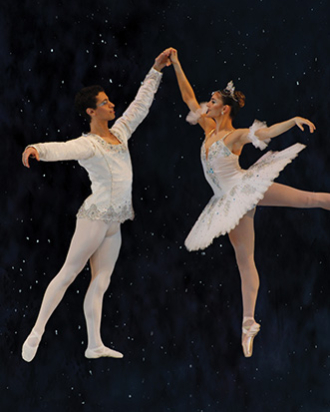 A pair of male and female ballet dancers dressed in all white pose together with pointed toes