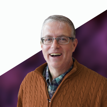 Steve Carignan wearing a rust colored sweater with a purple and white background.