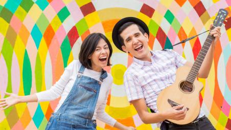 A man holding a guitar and woman smile with a colorful background 