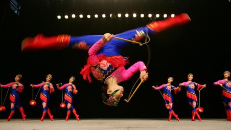 A girl in a red and blue costume doing a flip with dancers in the background 