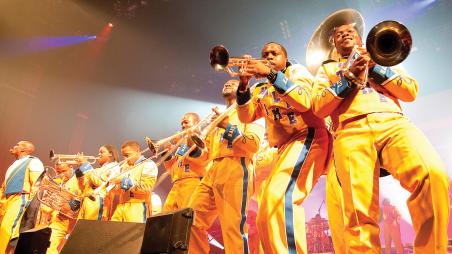A band in yellow uniforms holding instruments playing on a stage