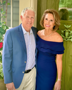 Terri and Steve in dress clothes stand and smile in front of their home.
